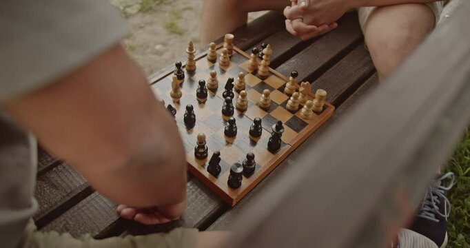 Two friends playing chess on a park bench. The chessboard is old and worn, suggesting many games have been played.