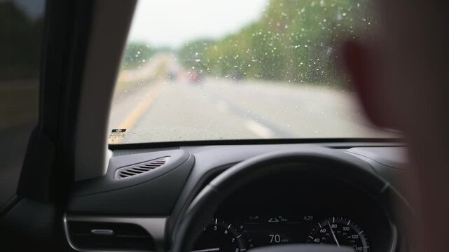POV from inside car on rainy day, showing blurred road ahead and windshield wipers in action, capturing the experience of driving in wet conditions. blurred road ahead and windshield wipers