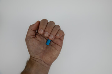 Almost closed caucasian male fist with a blue pill in the palm.  Hand against a white background.  Concept for regular medication use. 