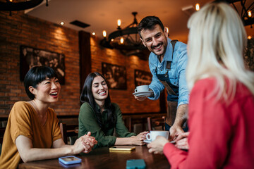Image of a waiter delivering drinks at a restaurant to a group of people sitting over a table.