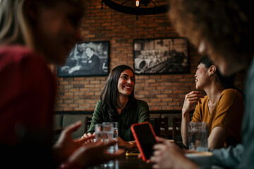 A group of multiracial friends browse social media on a smartphone in a lively cafe, sharing photos and updates