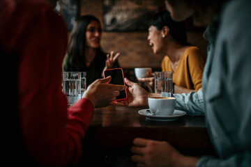 A group of happy friends browse social media on a smartphone in a lively cafe, sharing photos and updates