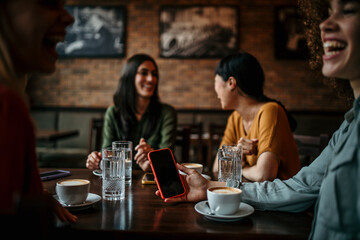 A group of happy friends browse social media on a smartphone in a lively cafe, sharing photos and updates