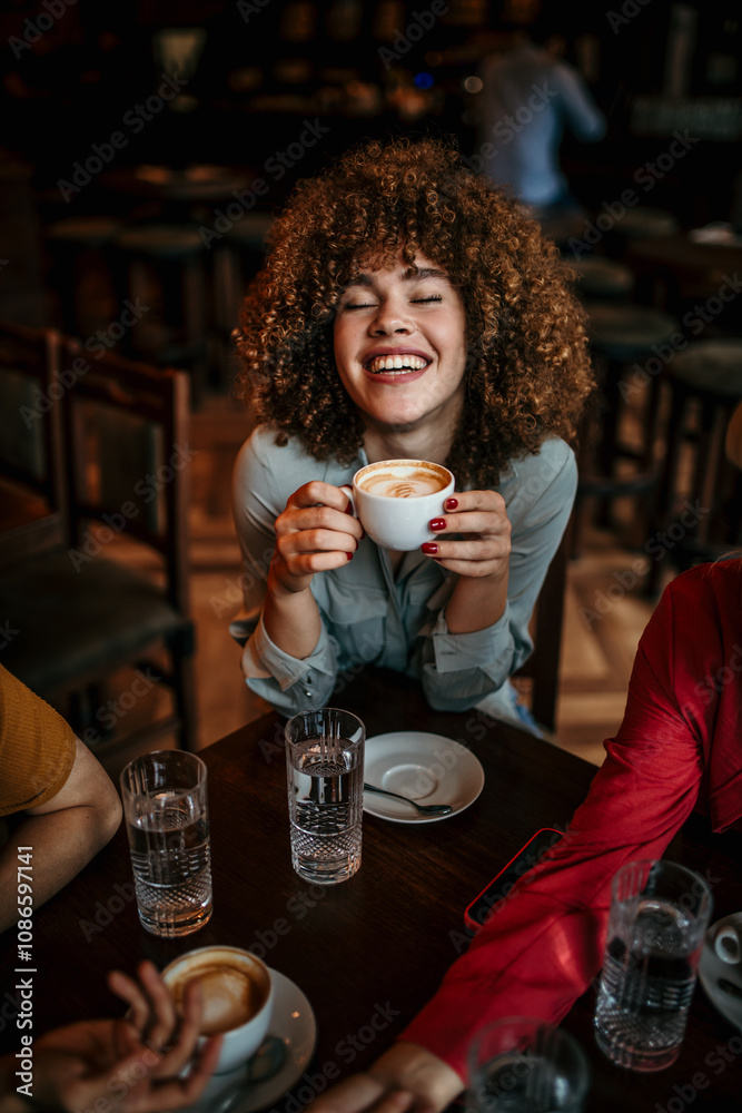 Wall mural A diverse group of friends enjoying some coffee together in a restaurant and talking. Focus on a smiling curly woman enjoying her cup of coffee