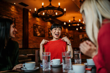 Carefree female friends have fun as they hang out together over coffee. Focus on a smiling Asian woman showing her new clothes