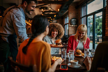 Young happy people having lunch together. An unrecognizable man passing burgers to his female...