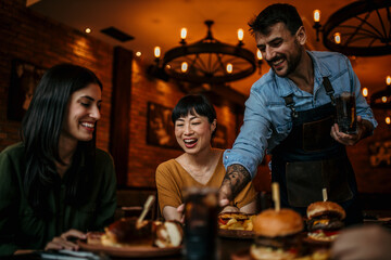 Waiter Serving Group Of Friends Meeting For Drinks And Food In Restaurant