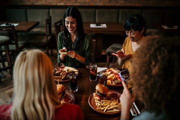 Multi-Cultural Group Of Friends Enjoying Night Out Taking Picture Of Food On Mobile Phone