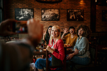 An unrecognizable man is photographing with a smartphone group of friends in the restaurant.