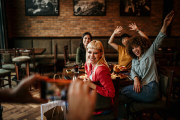 An unrecognizable man is photographing with a smartphone group of friends in the restaurant.
