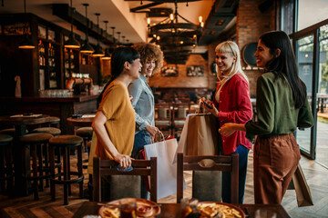 A group of smiling multiracial female friends leave the restaurant after a meal and drinks.