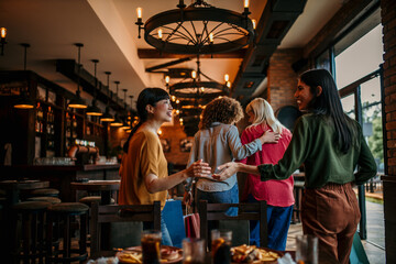 A group of smiling multiracial friends leave the restaurant after a meal and drinks.