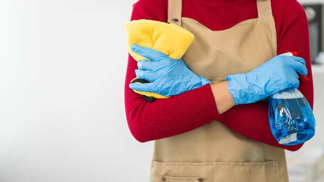 A young woman cleans her desk at home, using a disinfectant spray and a wipe. She ensures a hygienic and organized workspace, emphasizing cleanliness and personal health in her routine