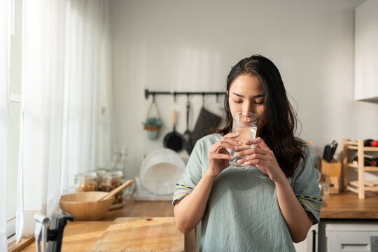 Asian young attractive woman drink a glass of water in kitchen at home. 