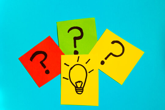Top view of sticky papers with question marks and drawn idea bulb on blue background, concept of question and ideas