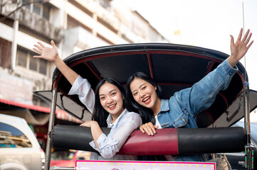 Two pretty Asian girl tourists enjoy exploring the city and taking a tuk-tuk ride in Thailand.