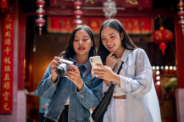 Two Asian female friends visit a Chinese shrine, checking photos on their smartphone and camera.