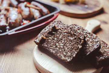 Rye flour bread with sunflower seeds on a wooden board against the background of grilled pans with fried sausages. Selected focus.