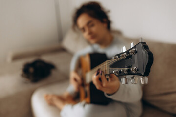 a woman tunes her guitar while sitting on the couch