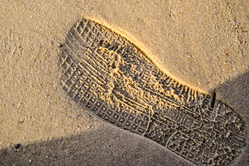 Close-up view of a detailed shoe print on a sandy beach, capturing the textured pattern and evoking ideas of footprints and exploration.