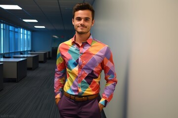 A man in a colorful shirt stands in front of a wall