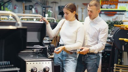 Young married couple chooses a new grill in a supermarket for their yard. High quality 4k footage - Powered by Adobe