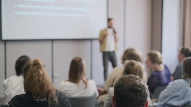 Group of people attentively listen to a speaker during a business presentation in a conference room setting.