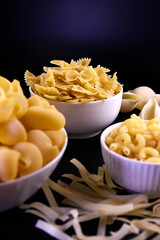 raw pasta in white plates on a black background. The paste has a textured surface and a delicate light yellow tint. Pasta background and texture.