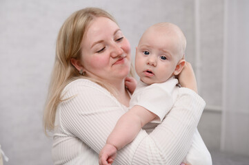 Happy mother holds her baby in an upright position, helps remove air from stomach after feeding, rocking. Woman enjoys tender moment, caring for infant. Concepts of motherhood and tenderness.Vertical