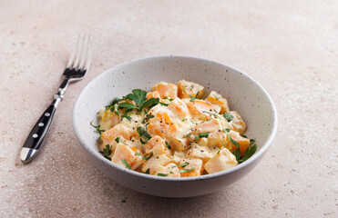 Bowl of pumpkin in sour cream sauce sprinkled with fresh parsley on beige textured stone table. Vegetarian food