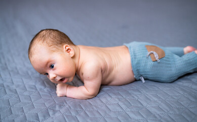 Baby in blue crawling on gray blanket. A young baby is crawling on a soft gray blanket, showing...