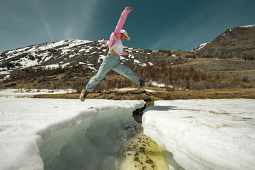 A man in bright clothes jumps over the ice with his hands up. Jump over a frozen lake. A tourist with his arms outstretched in the air against the background of mountains.