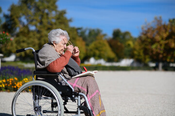 Portrait of elderly woman sitting in wheelchair and reading book. Semale senior spending warm...