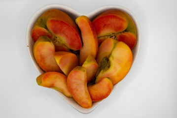 Cut in half and sliced kissabel apple in heart shaped bowl against white background. Hidden rose apples, pink inside apple