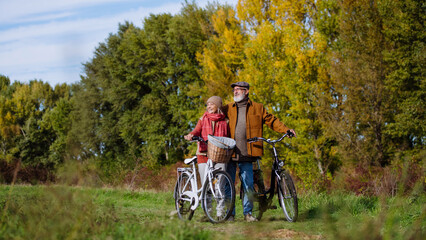 Lovely elderly couple on a walk in the forest, pushing their bikes side by side. Seniors in love on...