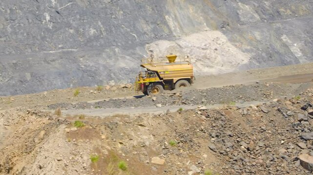 Big yellow mining truck watering a dirt road in a mine pit on a sunny day in Western Australia