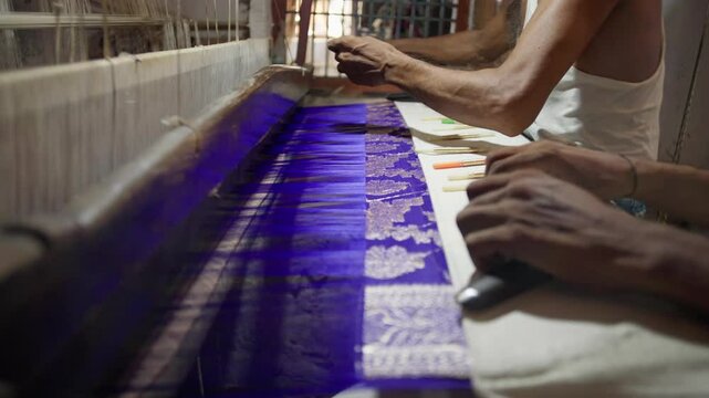 Close up profile view of Master artisan and assistant handweaving a Banarasi saree with intricate golden threadwork in Varanasi, India, showcasing the delicate craftsmanship 