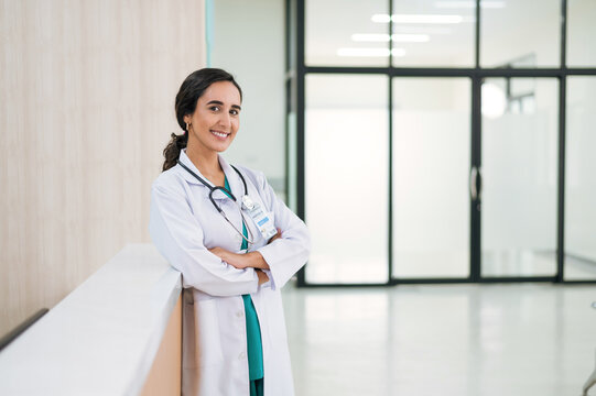 Profile photo of attractive smiling female doctor wearing white medical gown with stethoscope, standing in hospital corridor. Medicine and health care concept with copy space. looking at camera.