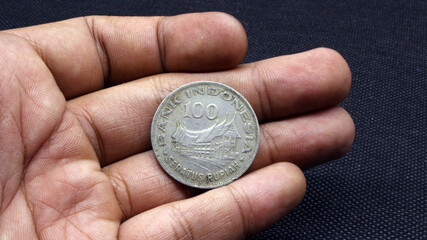 Hand holding an old coin of one hundred rupiah