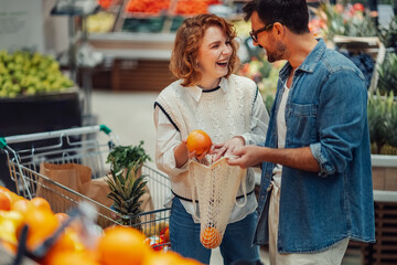 Happy couple buying oranges using reusable shopping bag at grocery store