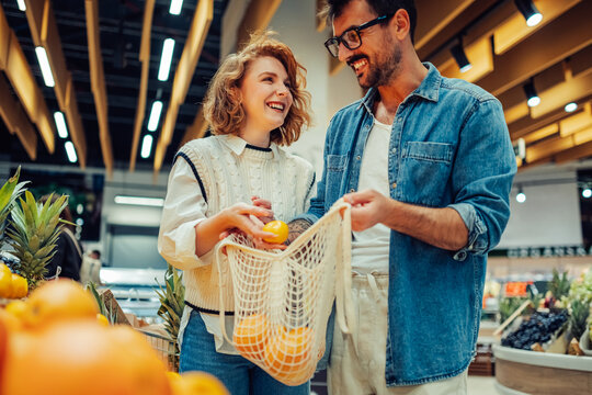 Happy couple choosing fresh oranges at grocery store using reusable bag