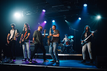 Fototapeta premium Music band playing live on stage during a concert under blue and purple lights