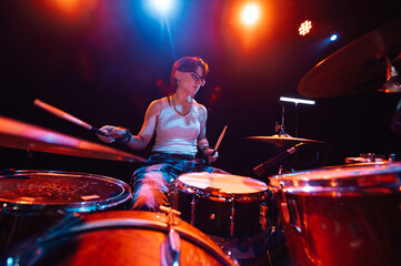 Female drummer performing energetically on stage with colorful lighting