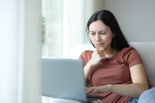 Suspicious asian woman checking laptop content at home