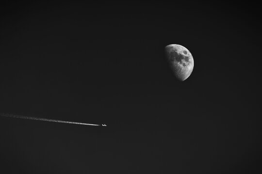Plane flying past the moon in monochrome.