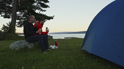 couple of trekkers friend waling together their meal at sunset in Norwegian fjord close to their camping spot