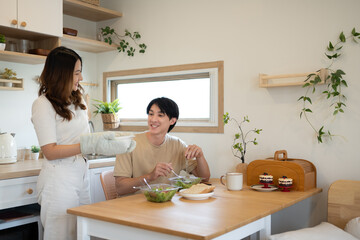 Young woman wearing an oven mitt serving a freshly prepared dish to her husband in a minimalist kitchen