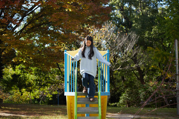 秋の公園で楽しく滑り台を遊んでいる小学生の女の子の様子