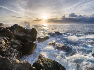 Waves crashing against rocky shoreline during sunset in the Azores Islands creating a peaceful coastal view