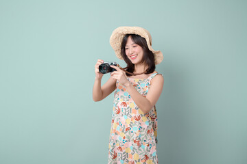 Happy Asian woman wearing casual dress and hat with camera on vacation or travel theme isolated on pastel green background. Travel and vacation concept. © Jirawatfoto